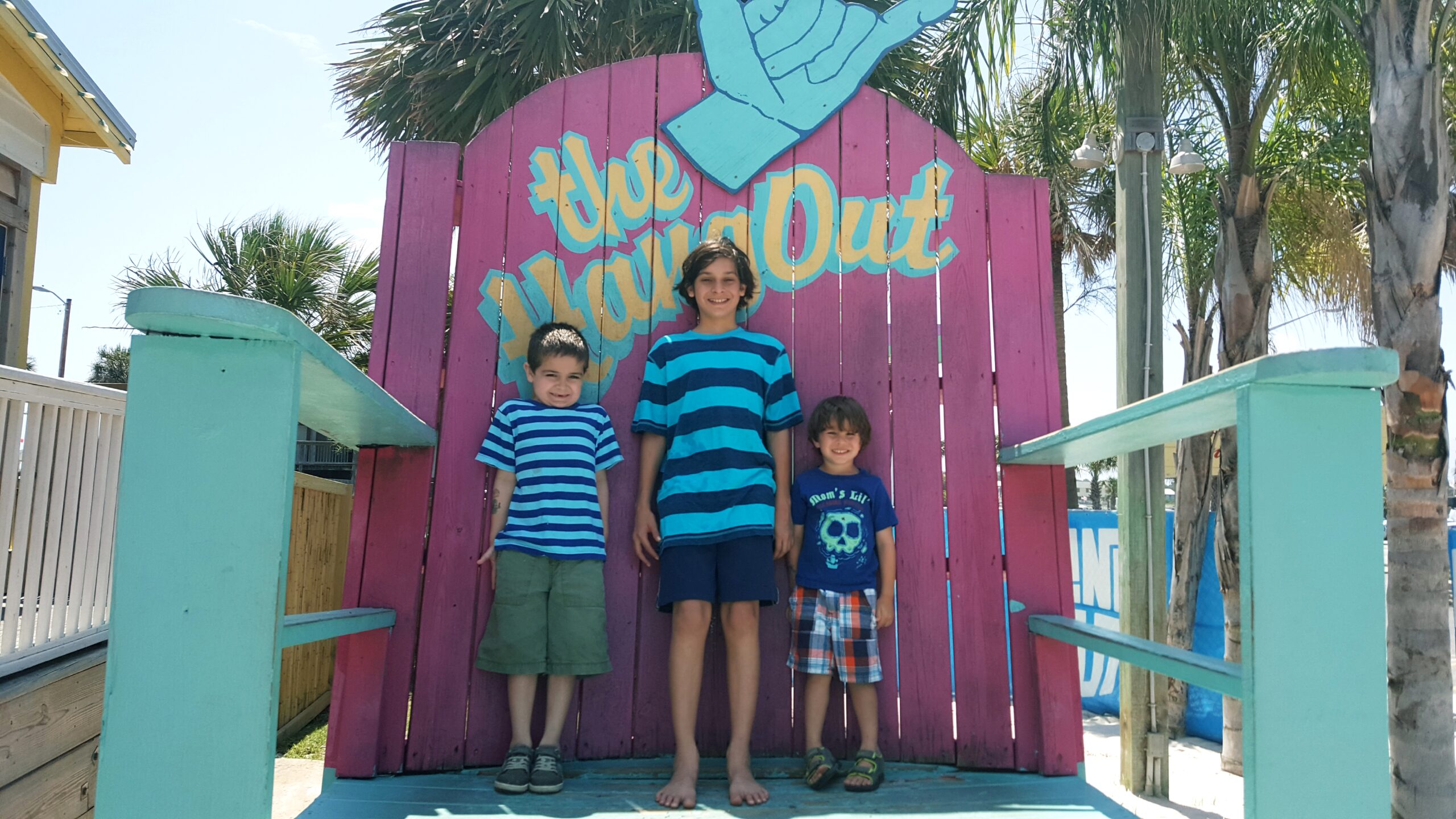 Three children standing together in front of a painted beach sign