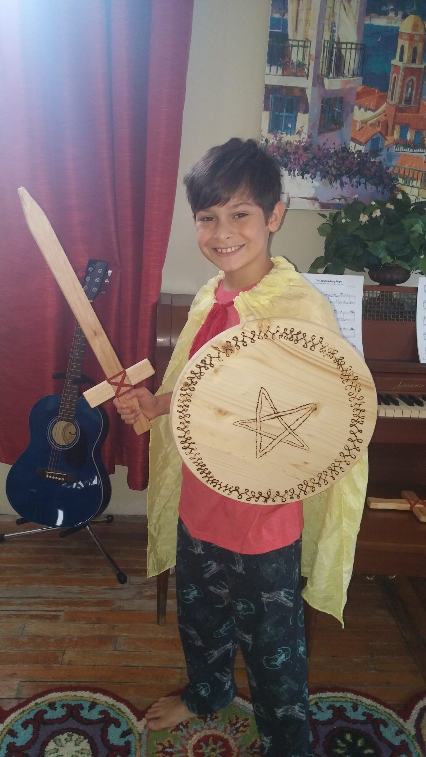 A boy in a golden cape with a wooden sword and a hand-painted shield