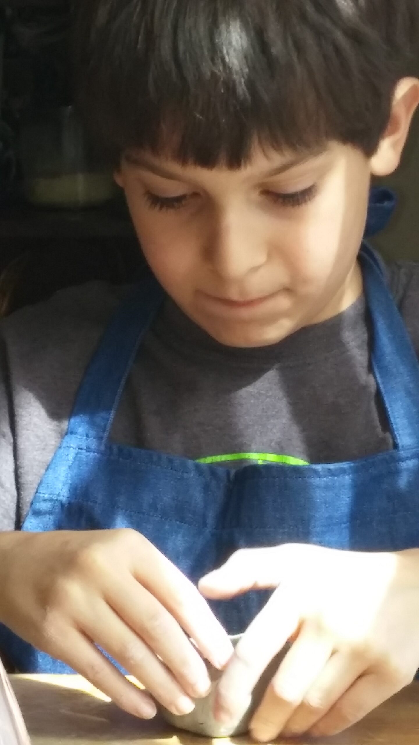A boy in a blue apron shaping clay with both hands
