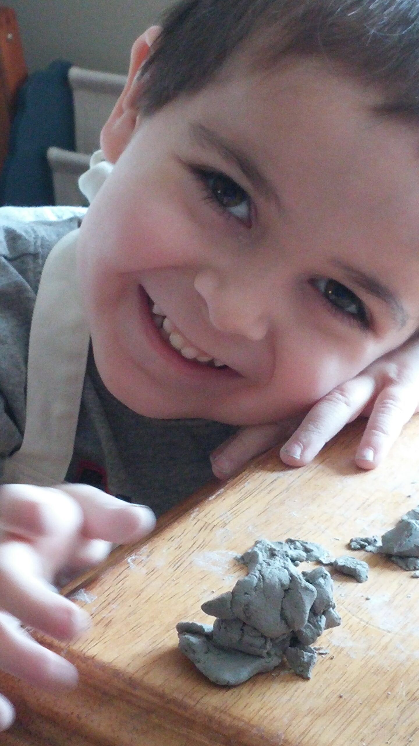 A smiling boy resting his head on the table beside his clay creation