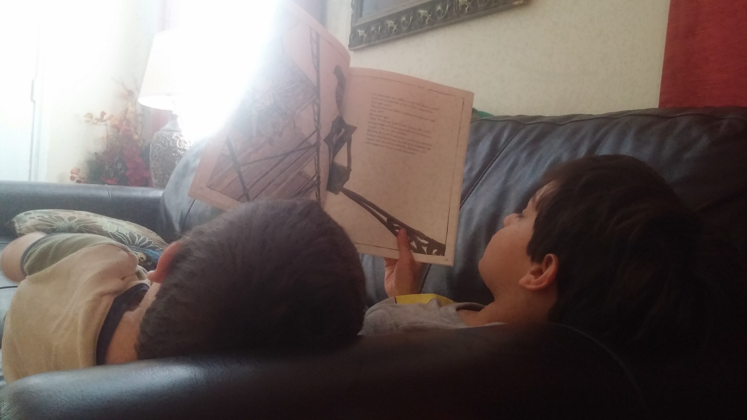 Two children curled up on the couch reading a picture book together