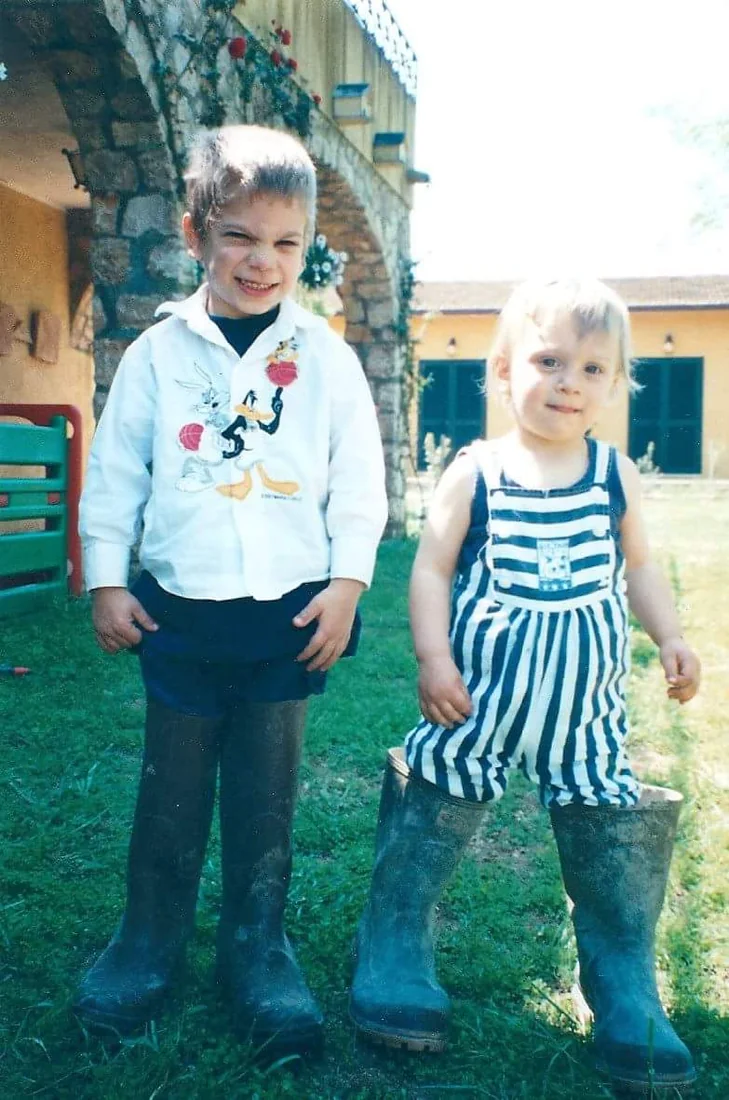 Two young children wearing grown-up rubber boots on the grass