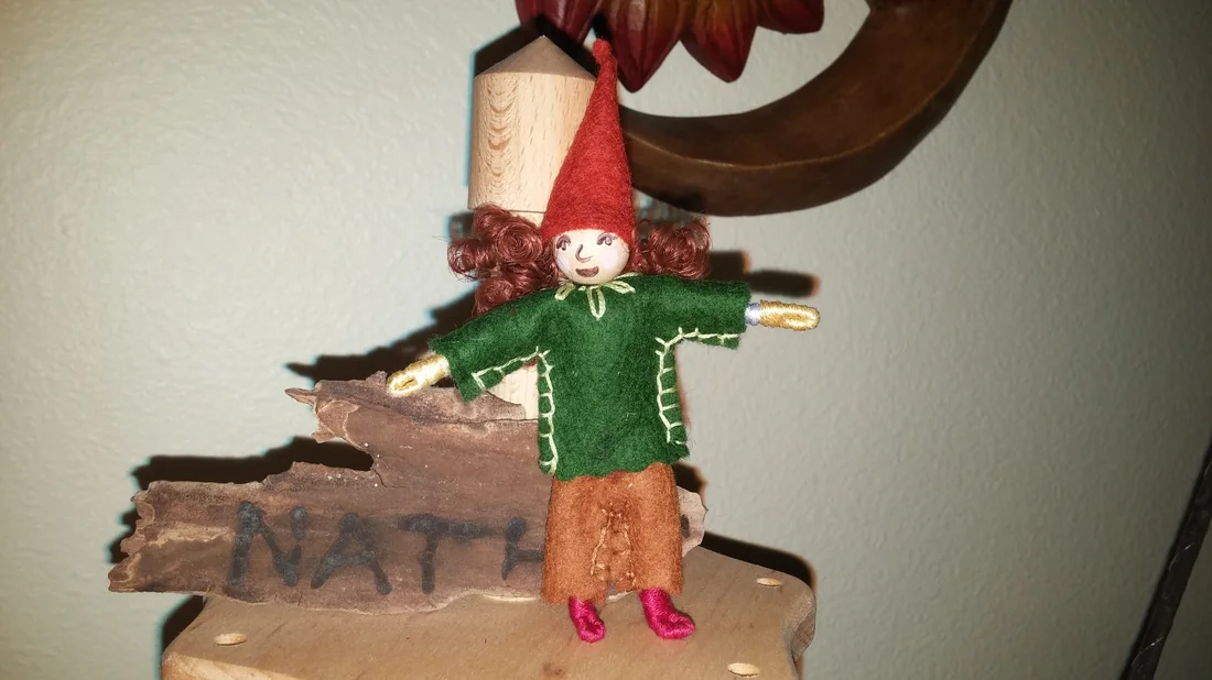 A felted gnome doll standing on a wooden shelf