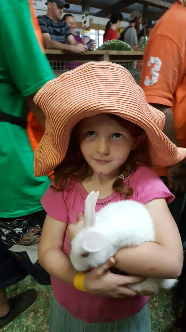 A girl in a wide straw hat holding a white rabbit