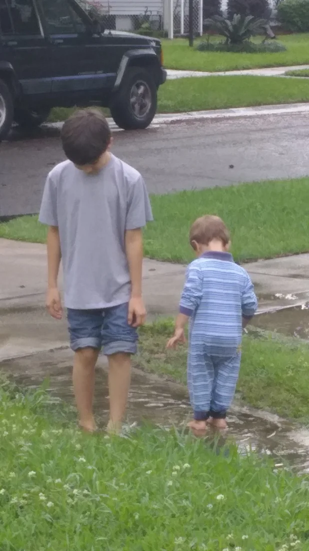 Two brothers standing barefoot in a puddle