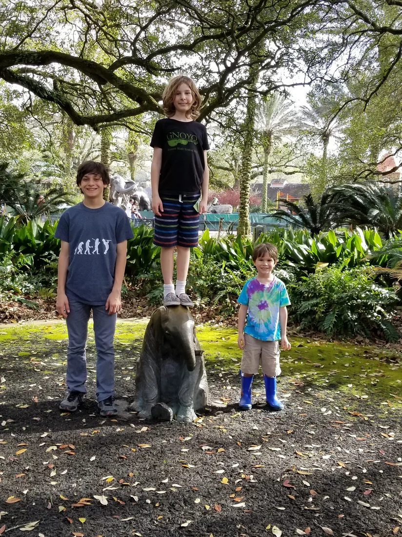 Three boys beside a bronze elephant under live oaks