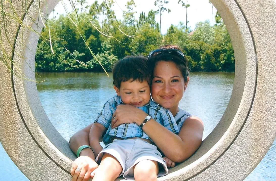 A mother holding her young son, framed in a stone circle by the water