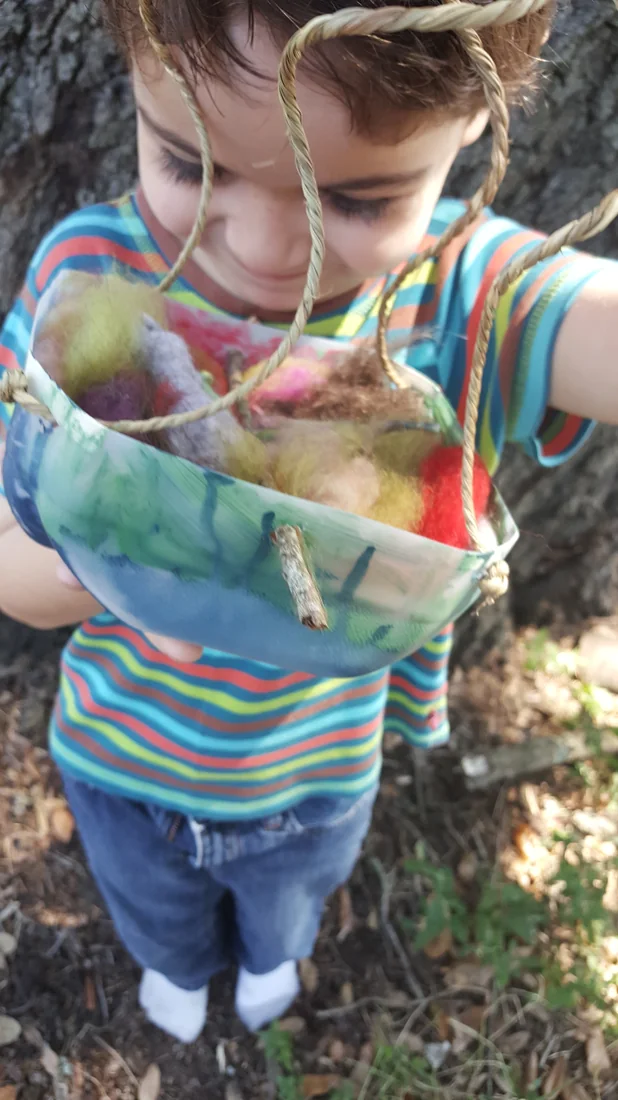 A child holding a painted basket filled with felted wool and twigs