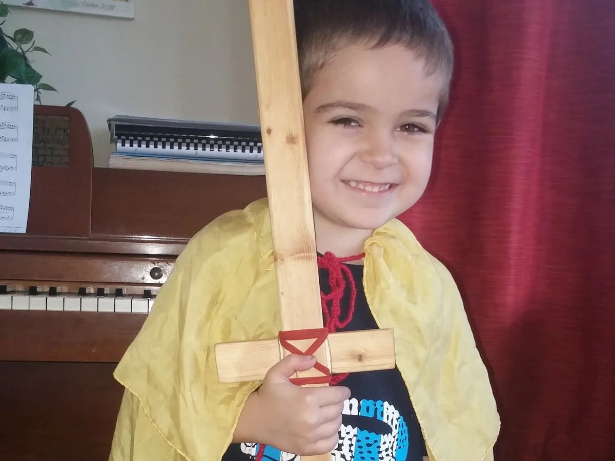 A child in a golden cape holding a wooden sword, dressed as one of Michael’s knights