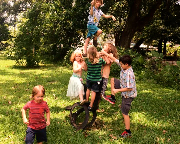 Children playing together on a tire swing under the oaks, one climbing the rope